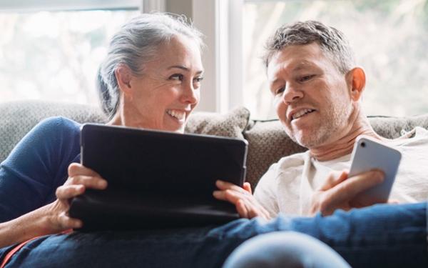 Une femme montre à un homme quelque chose sur sa tablette pendant que l'homme tient un téléphone