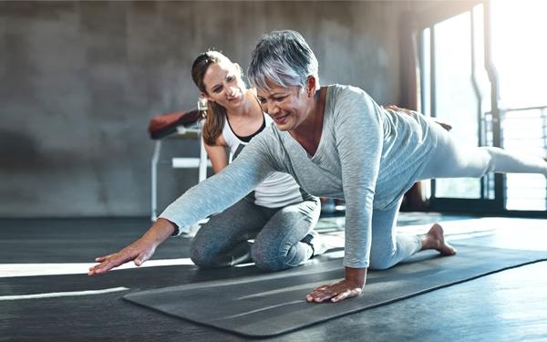 Une entraîneure personnelle aide une femme âgée à s'étirer sur un tapis de yoga
