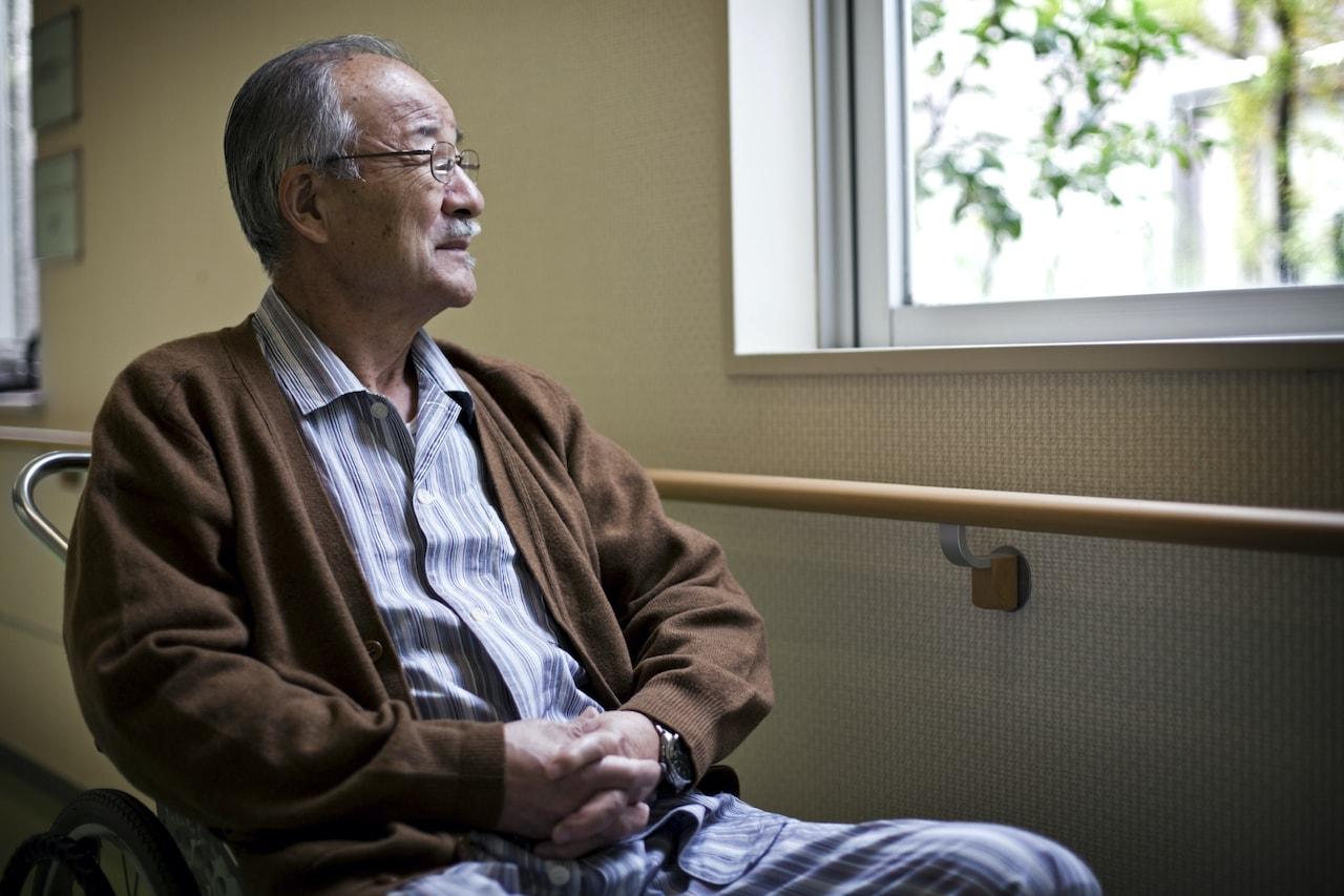 Assis près d'une fenêtre, un homme âgé regarde dehors